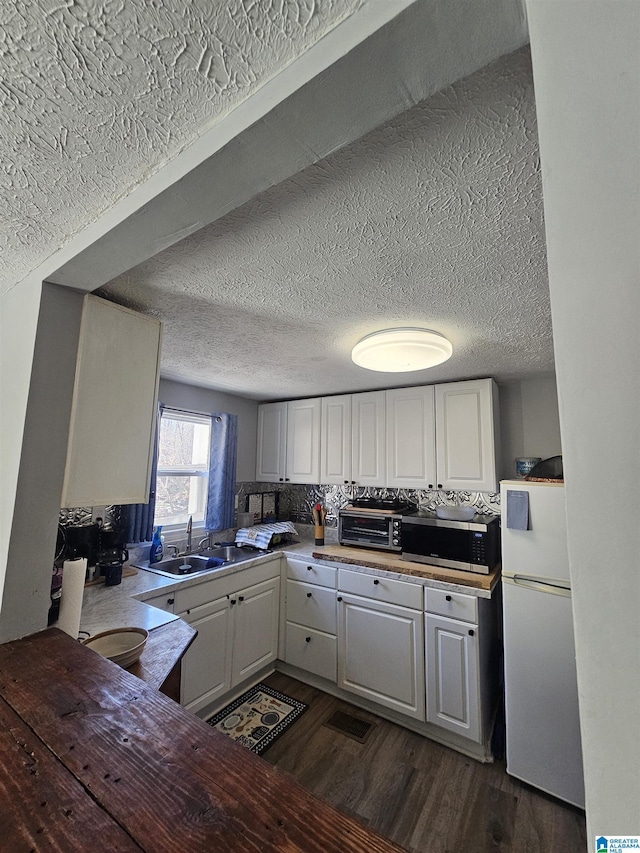 kitchen with decorative backsplash, dark wood-type flooring, sink, white refrigerator, and white cabinets