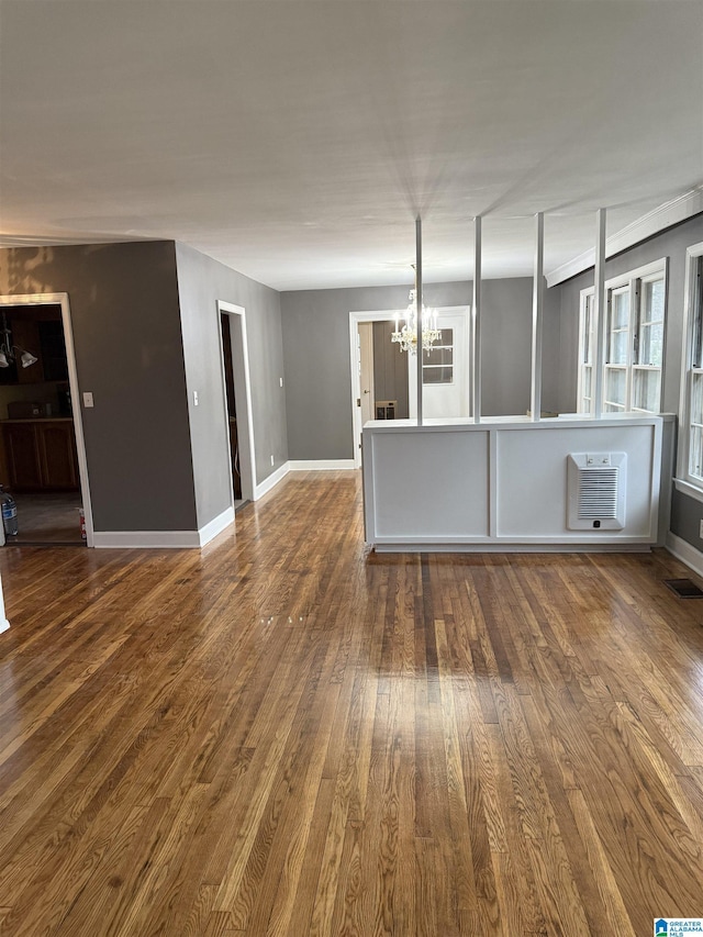 unfurnished living room featuring a wall mounted air conditioner, hardwood / wood-style flooring, an inviting chandelier, and heating unit