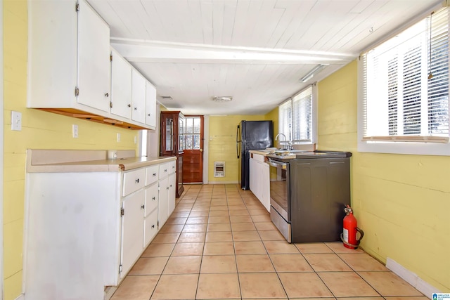 kitchen featuring white cabinetry, electric range, black fridge, heating unit, and light tile patterned floors