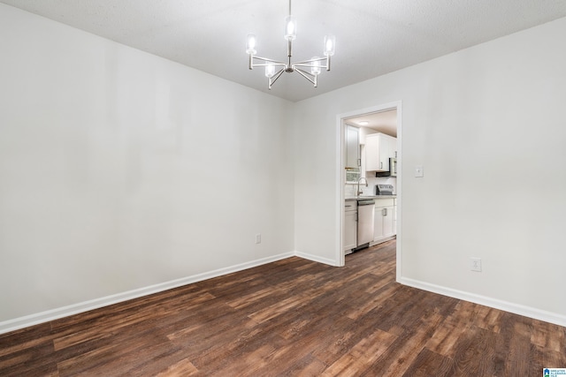 unfurnished room with sink, dark wood-type flooring, a textured ceiling, and an inviting chandelier