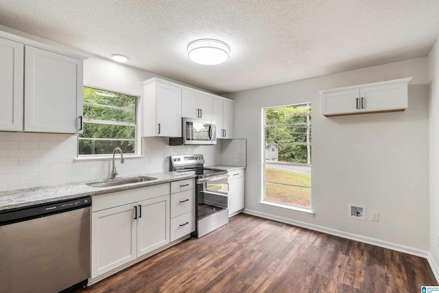 kitchen with sink, stainless steel appliances, light stone counters, backsplash, and white cabinets