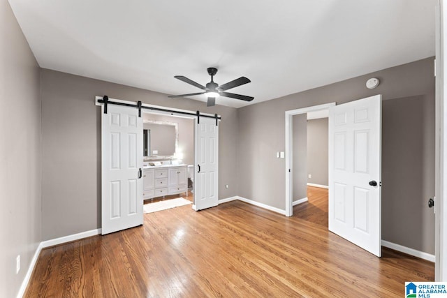 unfurnished bedroom featuring ceiling fan, a barn door, light hardwood / wood-style floors, and ensuite bath