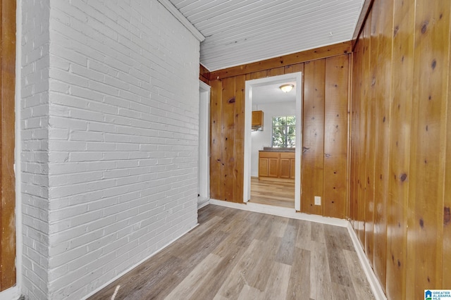 empty room featuring wood walls, light hardwood / wood-style flooring, and brick wall