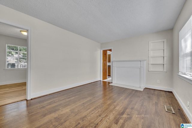 unfurnished living room with built in shelves, dark hardwood / wood-style flooring, and a textured ceiling