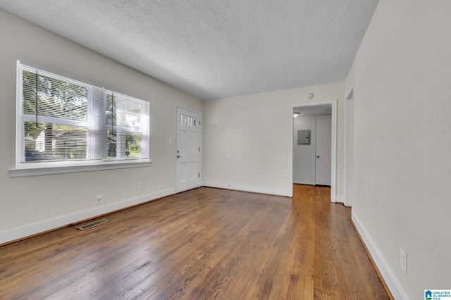 empty room with dark hardwood / wood-style floors, a textured ceiling, and electric panel