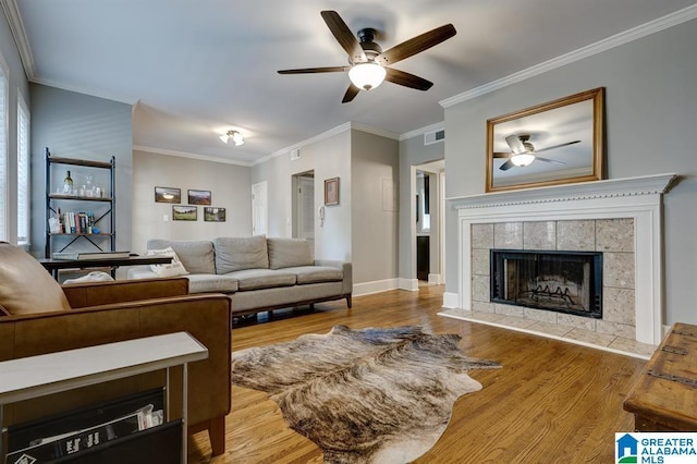 living room featuring a tiled fireplace, ceiling fan, hardwood / wood-style floors, and crown molding