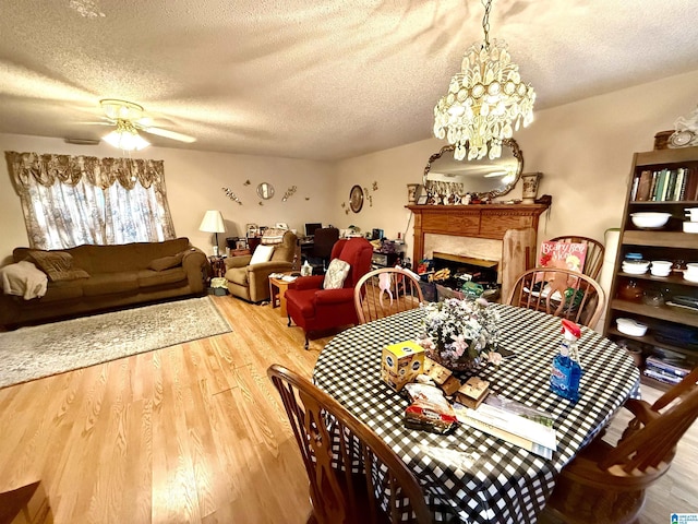 dining space with a fireplace, ceiling fan with notable chandelier, wood-type flooring, and a textured ceiling