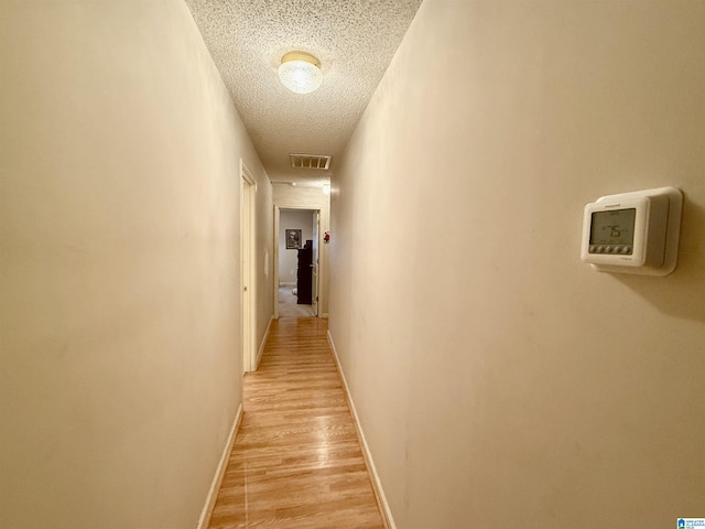 hall with a textured ceiling and light wood-type flooring