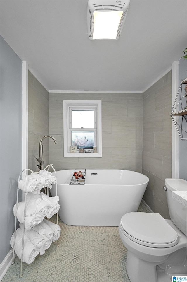 bathroom with tile patterned floors, a tub to relax in, toilet, and tile walls