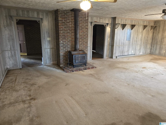 unfurnished living room with a wood stove, ceiling fan, electric panel, a textured ceiling, and dark carpet