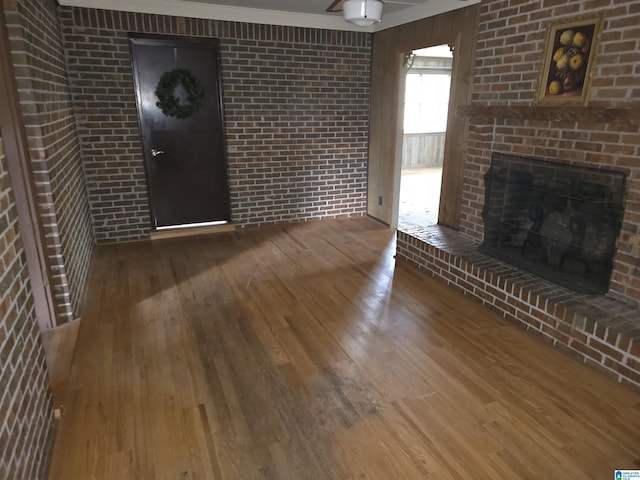 unfurnished living room with hardwood / wood-style flooring, brick wall, and a brick fireplace