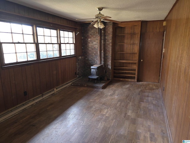 unfurnished room with a textured ceiling, a wood stove, ceiling fan, and wooden walls