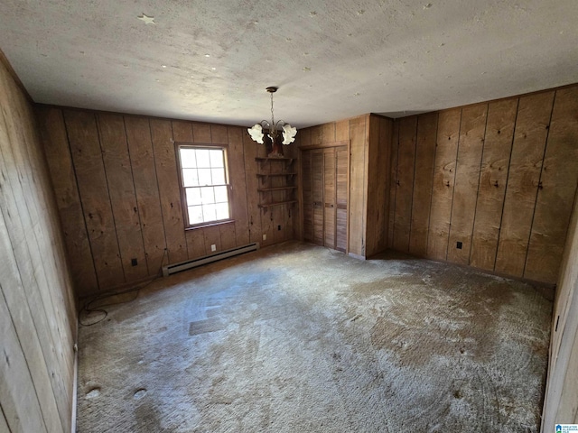 carpeted empty room featuring wooden walls, a chandelier, a textured ceiling, and a baseboard heating unit