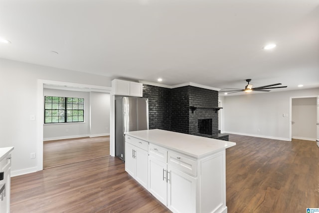 kitchen featuring dark wood-type flooring, white cabinets, a brick fireplace, ceiling fan, and stainless steel fridge