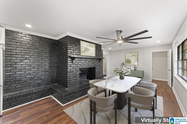 dining room featuring ceiling fan, crown molding, wood-type flooring, and a brick fireplace