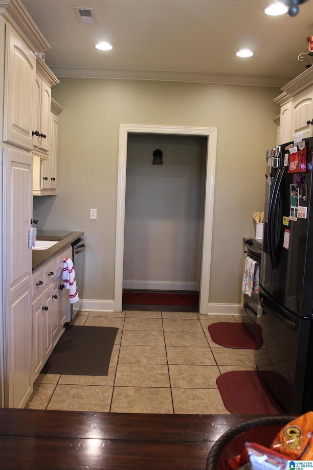 kitchen with cream cabinets, ornamental molding, stainless steel dishwasher, light tile patterned floors, and black fridge