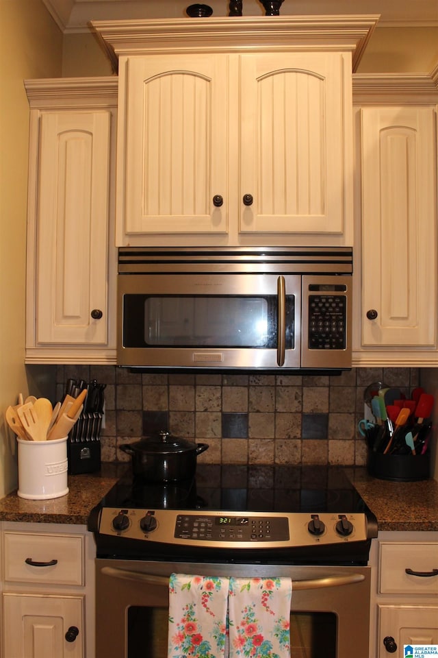 kitchen featuring tasteful backsplash, white cabinetry, dark stone counters, ornamental molding, and stainless steel appliances