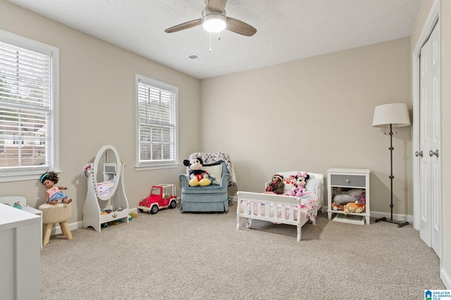 carpeted bedroom with ceiling fan, a crib, and a textured ceiling