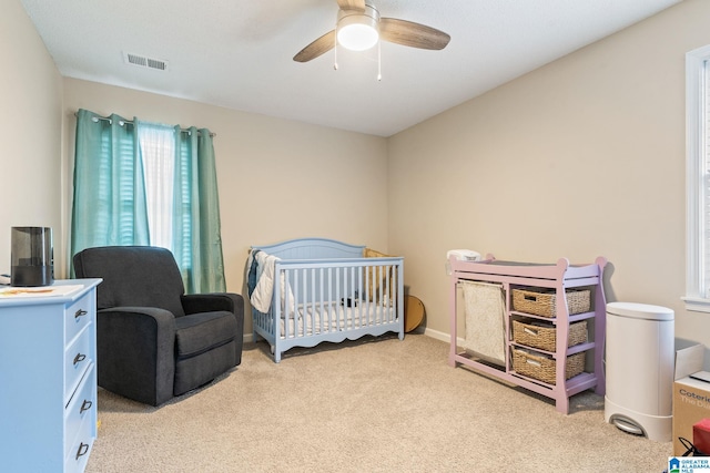 carpeted bedroom with ceiling fan and a nursery area