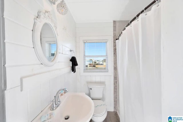 bathroom with a shower with curtain, wooden walls, sink, and toilet