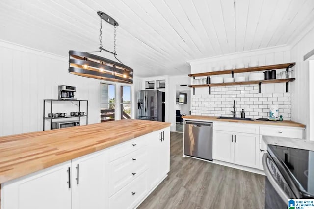 kitchen featuring wooden counters, stainless steel appliances, sink, pendant lighting, and white cabinetry