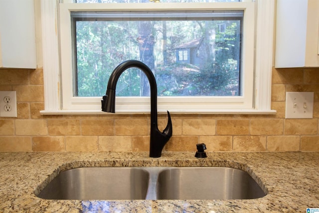 details featuring tasteful backsplash, light stone countertops, sink, and white cabinetry