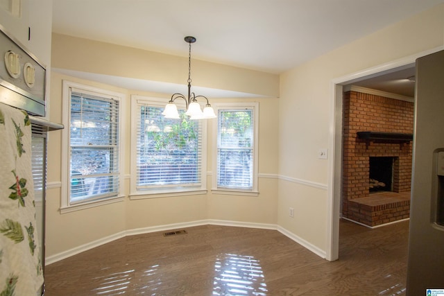 unfurnished dining area featuring dark wood-type flooring, a fireplace, a chandelier, and ornamental molding