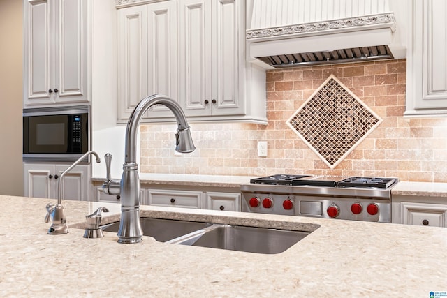 kitchen featuring light stone countertops, stainless steel microwave, sink, tasteful backsplash, and premium range hood