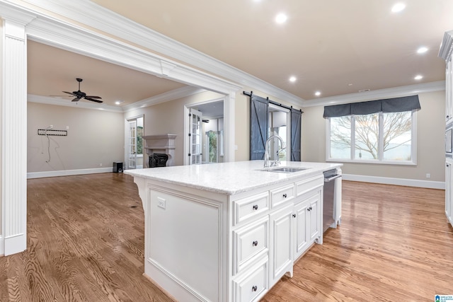 kitchen with white cabinets, sink, ceiling fan, a barn door, and an island with sink