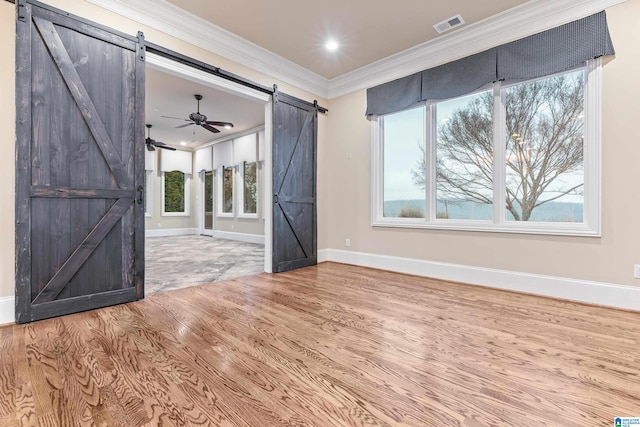 empty room featuring ceiling fan, a barn door, wood-type flooring, and ornamental molding