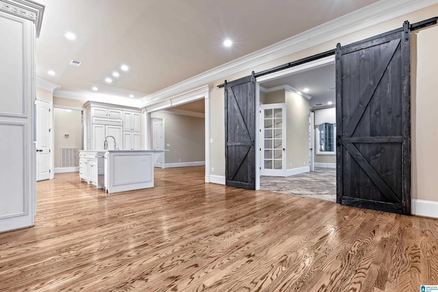 unfurnished living room featuring light wood-type flooring, a barn door, ornamental molding, and sink