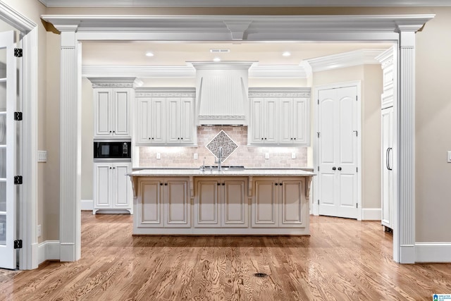 kitchen featuring black microwave, a kitchen island with sink, and ornamental molding