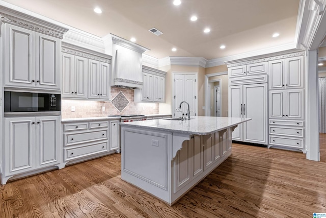 kitchen with light stone counters, a breakfast bar, sink, built in appliances, and a center island with sink