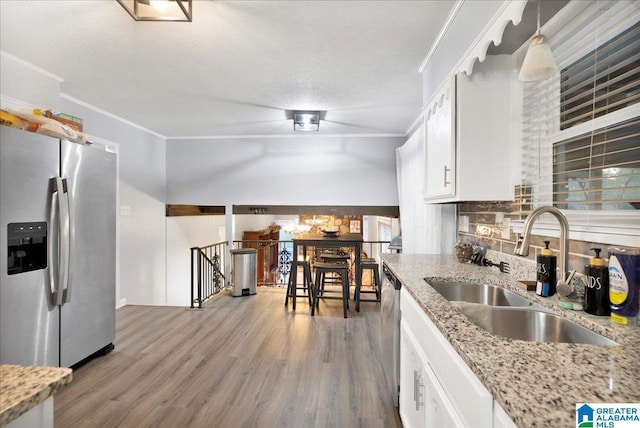 kitchen featuring appliances with stainless steel finishes, light stone counters, crown molding, sink, and white cabinets