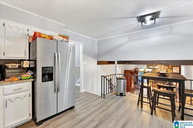 kitchen with white cabinets, light hardwood / wood-style flooring, stainless steel fridge, ornamental molding, and a textured ceiling