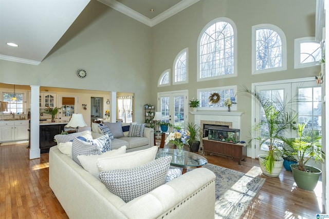 living room featuring light wood-type flooring, ornamental molding, a high ceiling, and a tiled fireplace