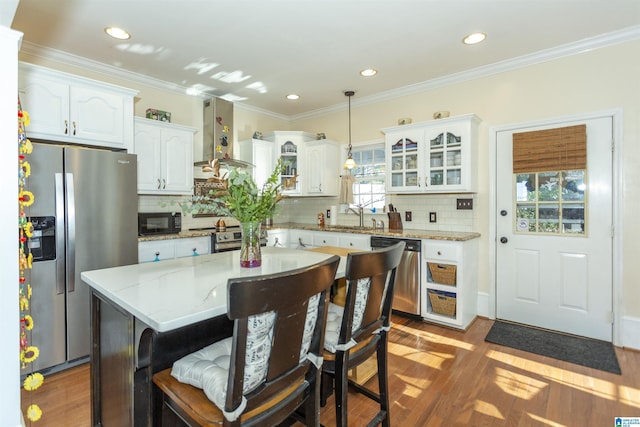 kitchen featuring hanging light fixtures, wall chimney range hood, a kitchen island, white cabinets, and appliances with stainless steel finishes