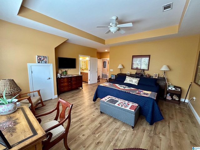 bedroom featuring ceiling fan, ensuite bathroom, and a tray ceiling