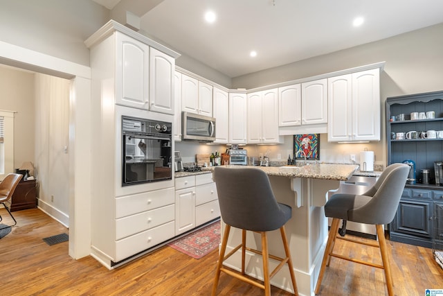 kitchen featuring black oven, light hardwood / wood-style floors, a kitchen breakfast bar, and white cabinetry