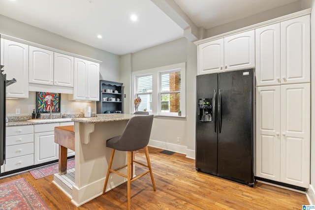 kitchen featuring white cabinetry, light stone countertops, black refrigerator with ice dispenser, light hardwood / wood-style flooring, and a kitchen island