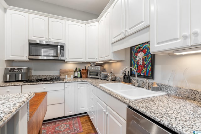 kitchen with white cabinets, appliances with stainless steel finishes, light stone countertops, and sink