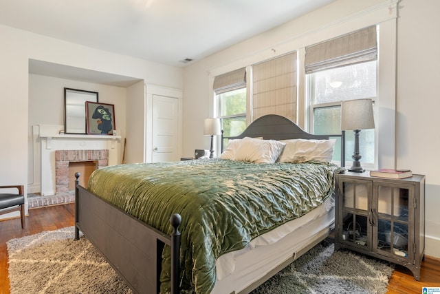 bedroom with wood-type flooring and a brick fireplace