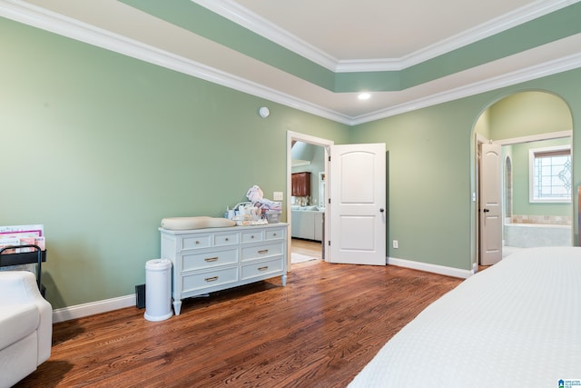 bedroom featuring a raised ceiling, connected bathroom, dark hardwood / wood-style flooring, and ornamental molding