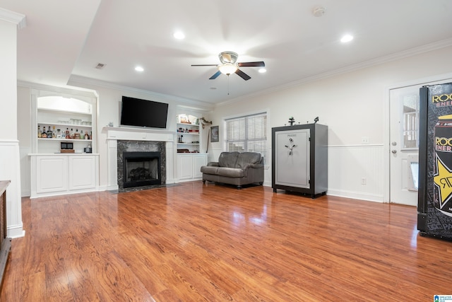 unfurnished living room featuring built in shelves, a fireplace, crown molding, and ceiling fan