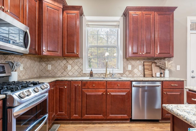 kitchen featuring sink, decorative backsplash, light stone countertops, light wood-type flooring, and stainless steel appliances