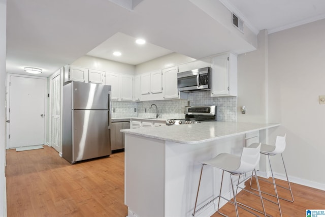 kitchen featuring white cabinets, sink, appliances with stainless steel finishes, a kitchen bar, and kitchen peninsula