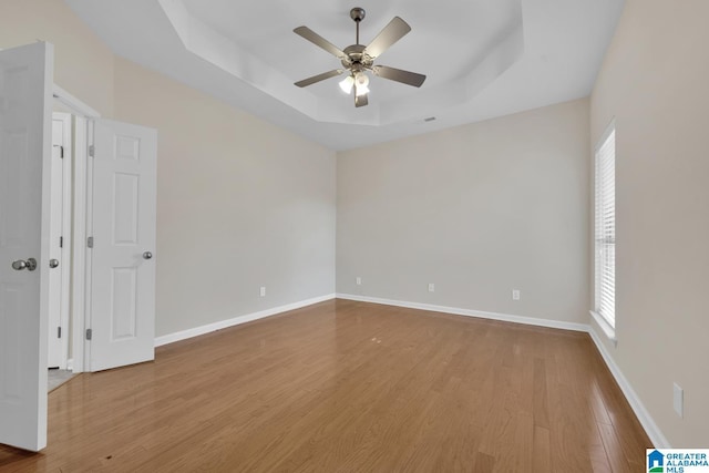 unfurnished room featuring ceiling fan, a raised ceiling, and light wood-type flooring