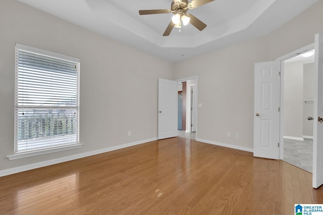 empty room featuring ceiling fan, light hardwood / wood-style flooring, and a tray ceiling