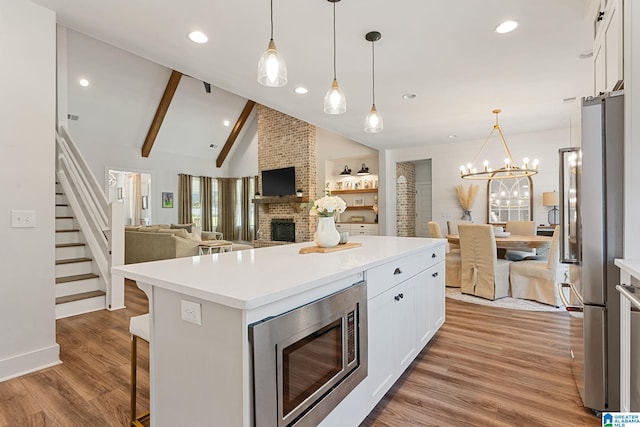 kitchen with a brick fireplace, appliances with stainless steel finishes, beamed ceiling, a kitchen bar, and white cabinetry