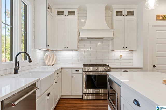 kitchen featuring light stone countertops, custom range hood, stainless steel appliances, sink, and white cabinets